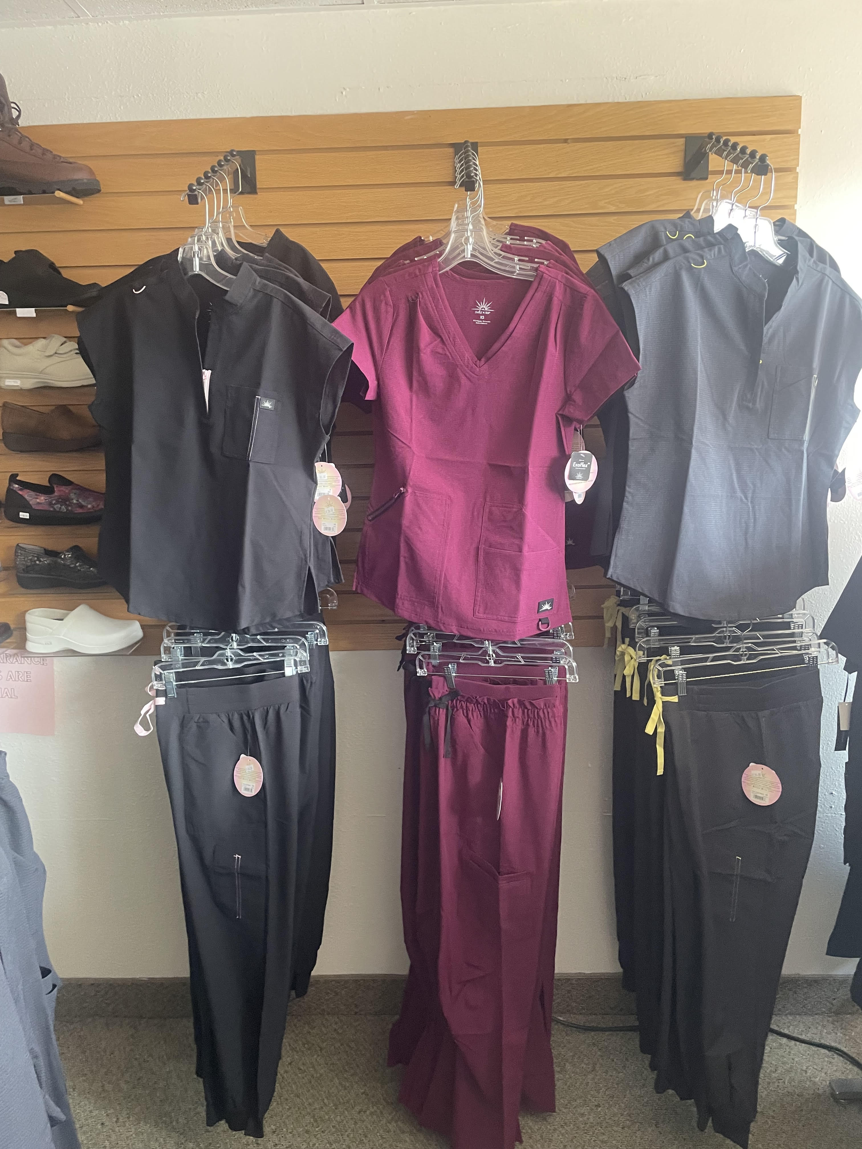 Black, burgundy, and gray scrub sets displayed on the slatwall at Scrub JCT